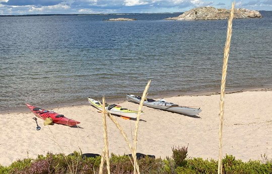 Tre kajaker på strand vid skärgårdens vatten