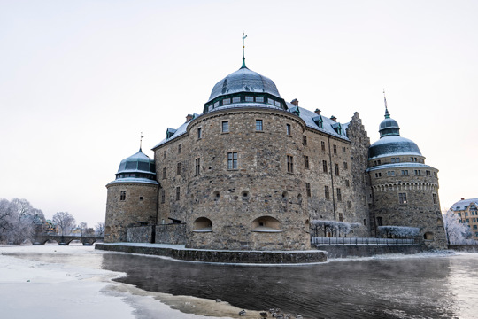 Örebro slott i vinterskrud, omgivet av frusen vattenyta och snötäckta träd.