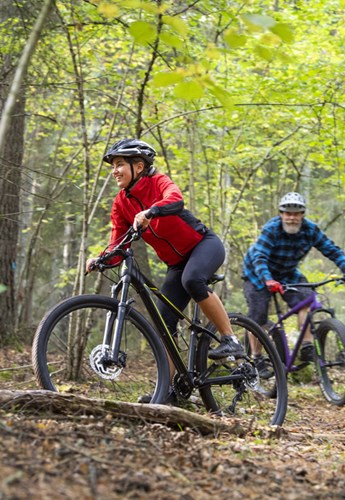 Tre mountainbikecyklister cyklar på en lövtävkt stig genom skogen.